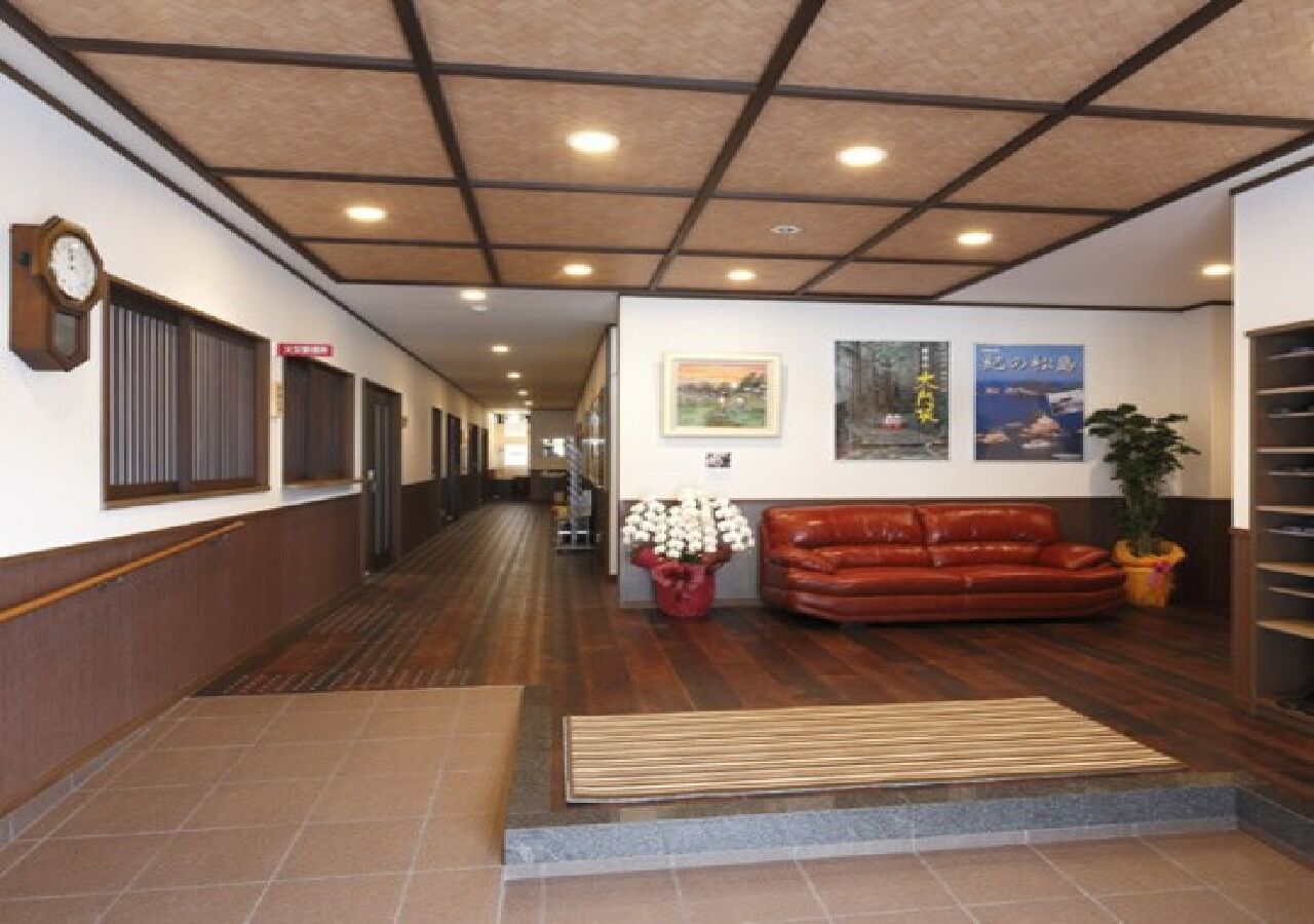 Ein Flur mit Holzboden, einem braunen Ledersofa, einer roten Blumenkomposition und einer Uhr an der Wand.