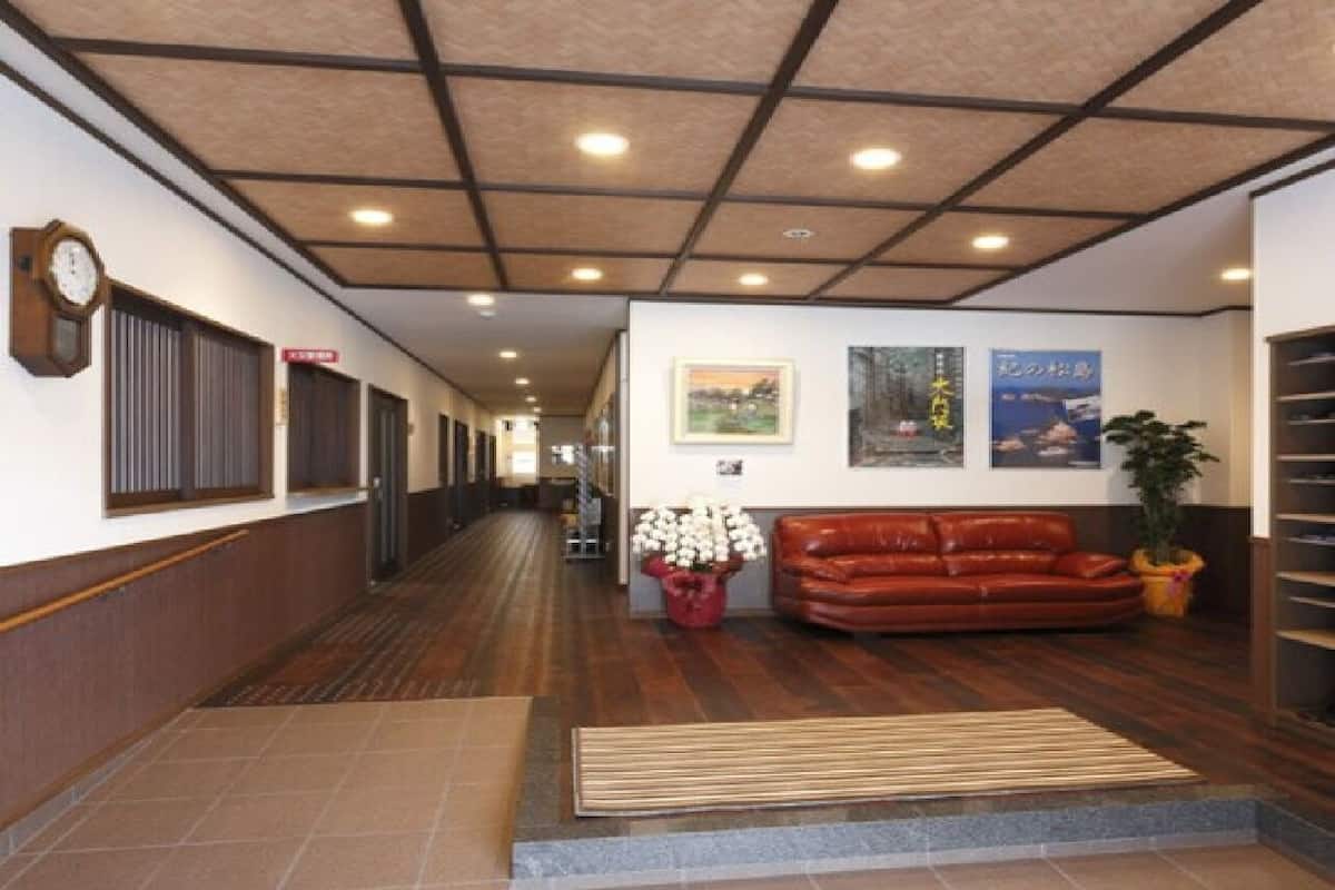 Un couloir avec un plancher en bois, un canapé en cuir marron, un arrangement floral rouge et une horloge au mur.