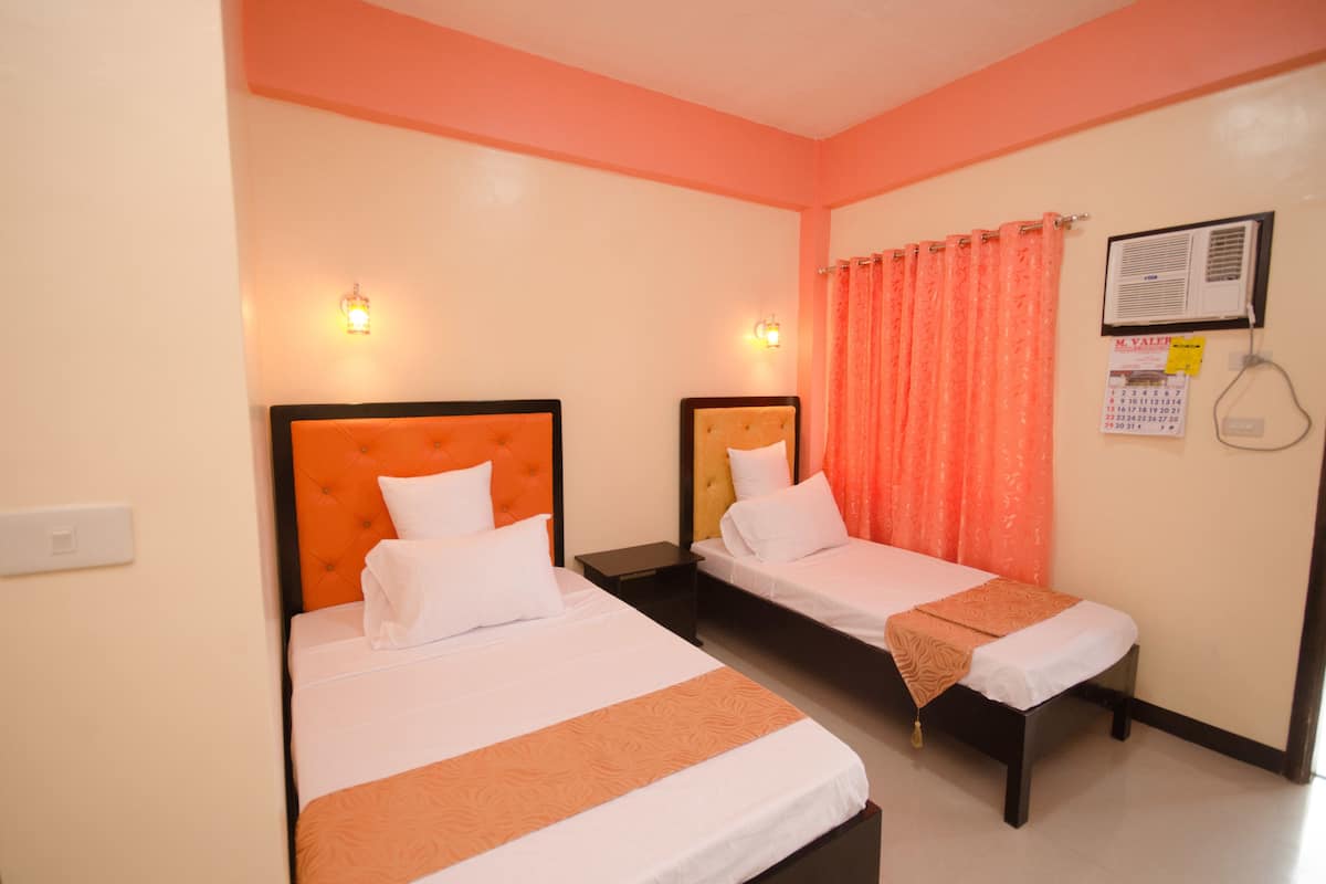 Two single beds with orange headboards in a room with peach walls and a window with orange curtains.