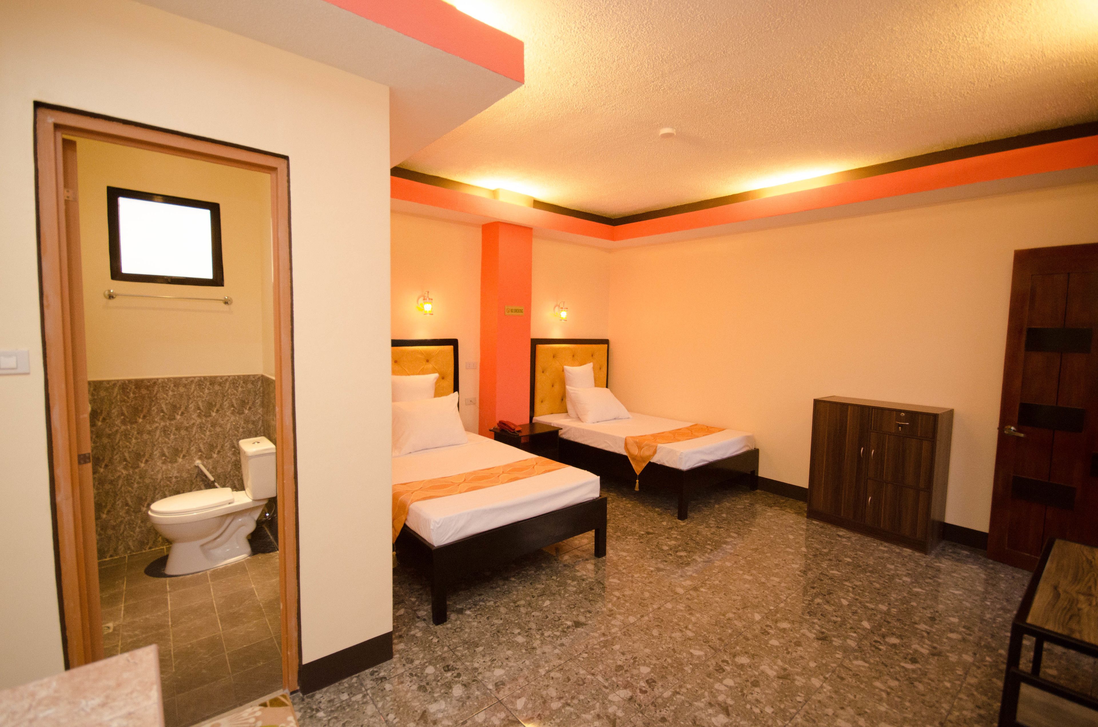 Habitación de hotel con dos camas individuales, un armario de madera, piso de baldosas de mármol y un inodoro en un rincón.
