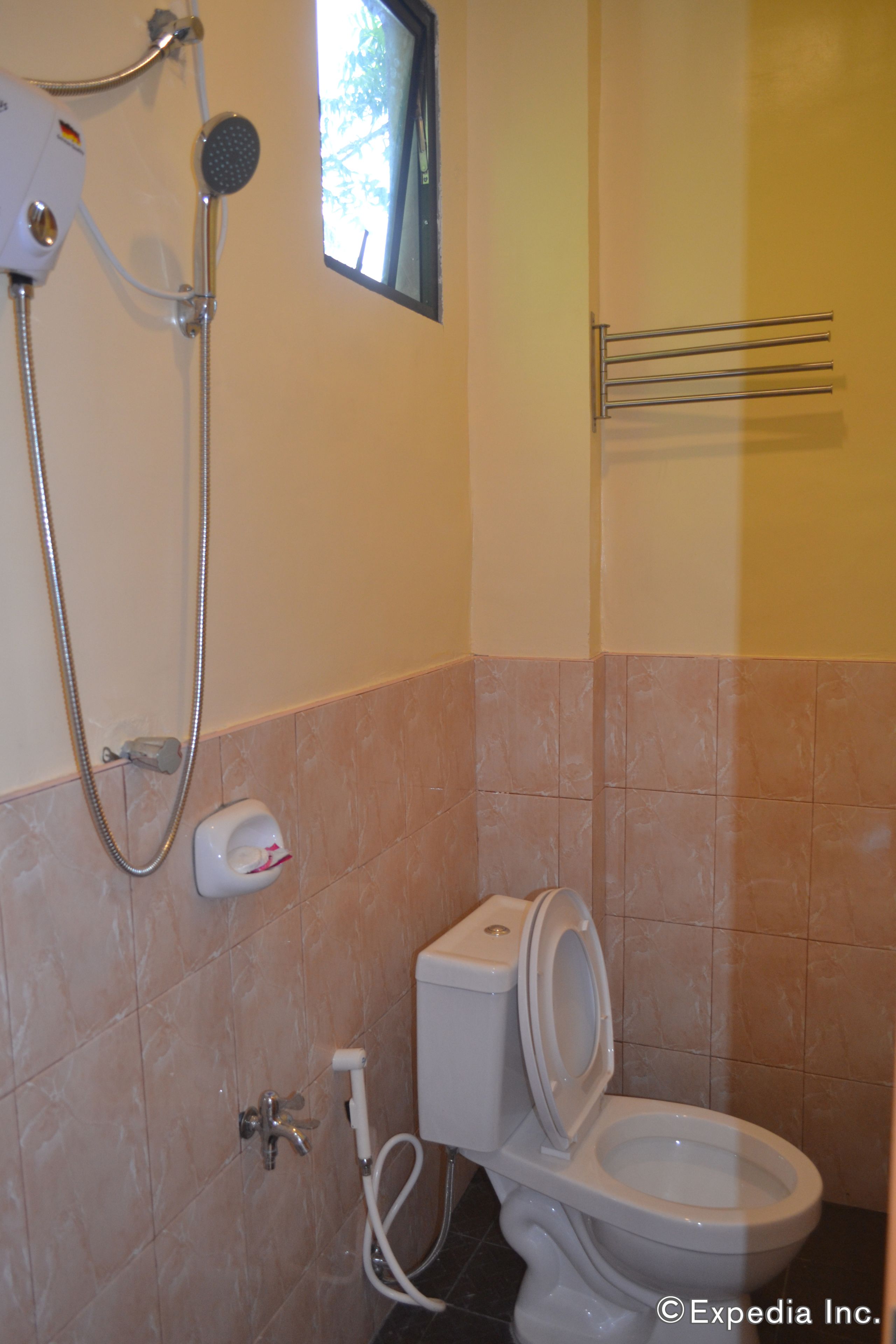Un baño con inodoro, cabezal de ducha manual y un perchero para toallas.