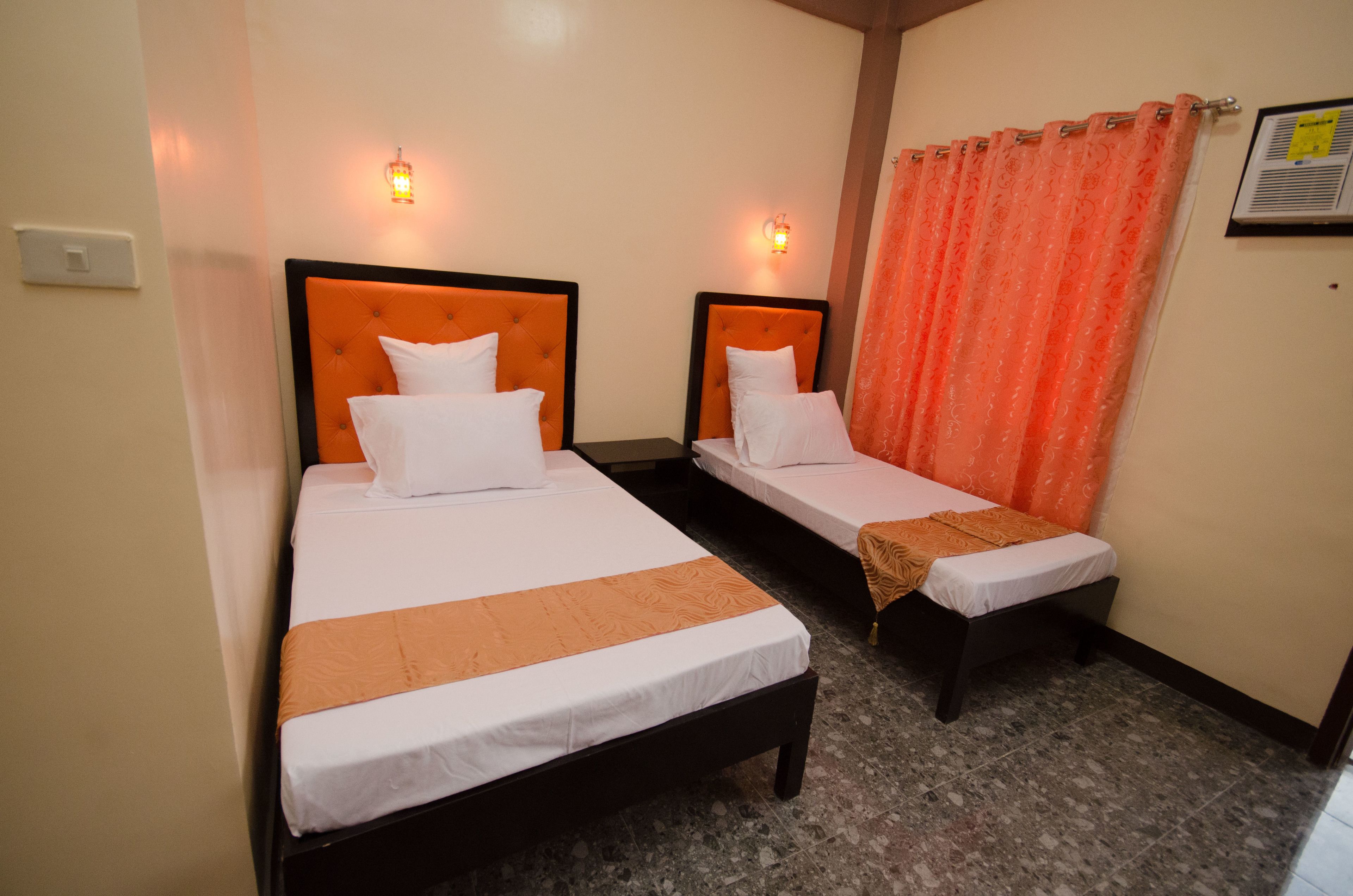 A hotel room with two single beds, each with a headboard and a bedside table.