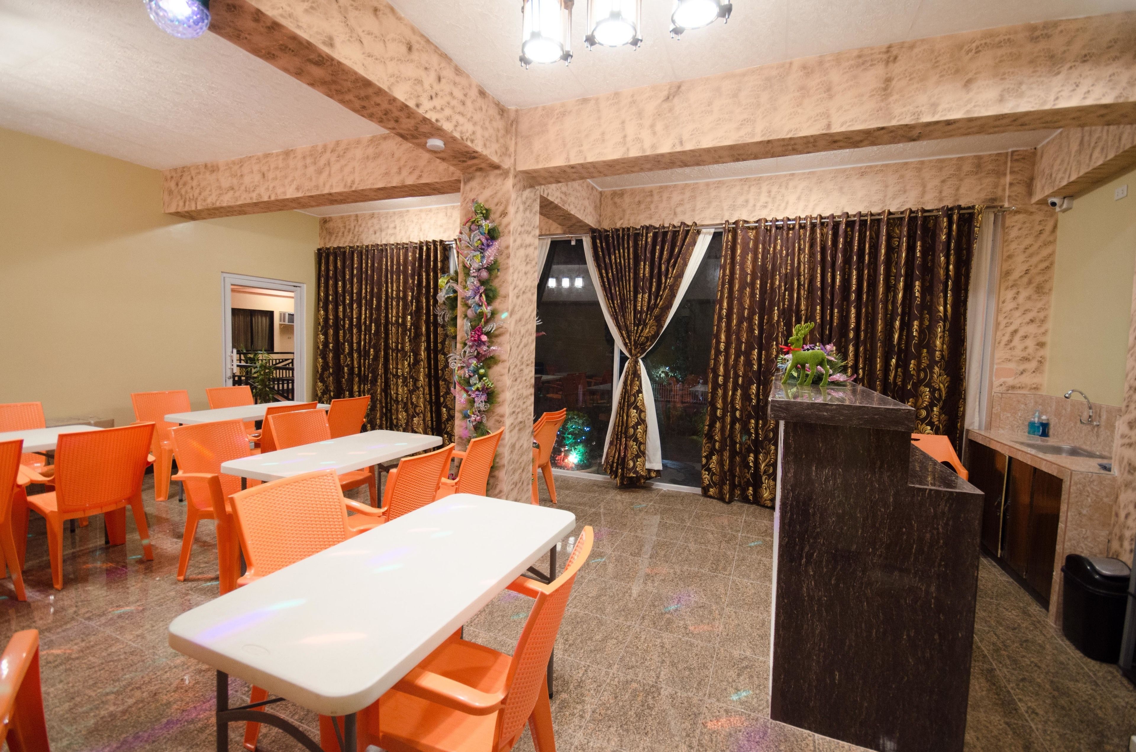 A dining area with orange chairs and white tables, a podium, and a view through a window with curtains.
