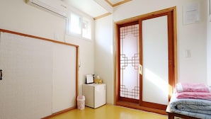 Una habitación con puerta corredera, una cama, una mesita y un aire acondicionado.