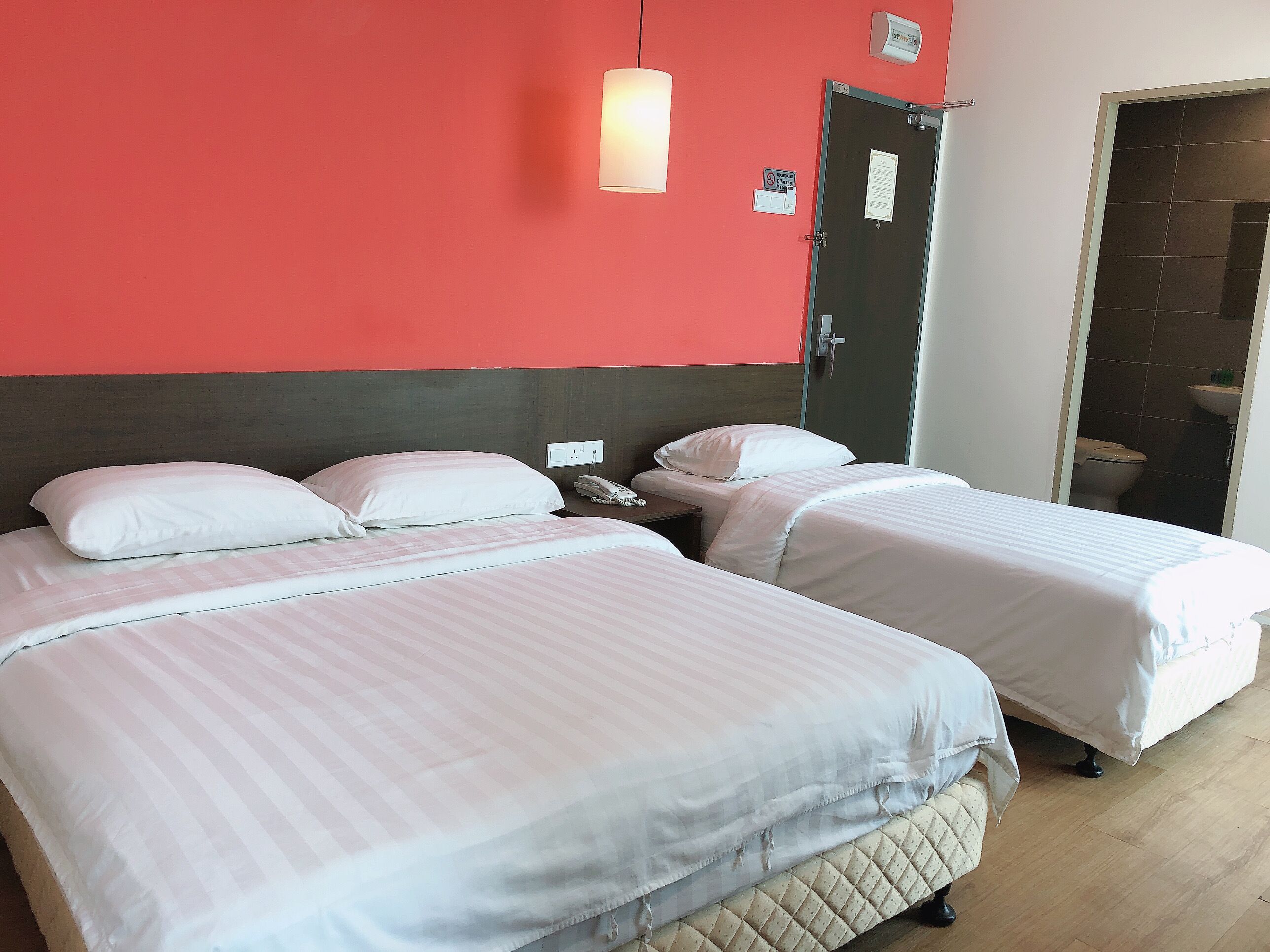 A hotel room with two beds, a red wall, a door, and a bathroom visible through an open door.