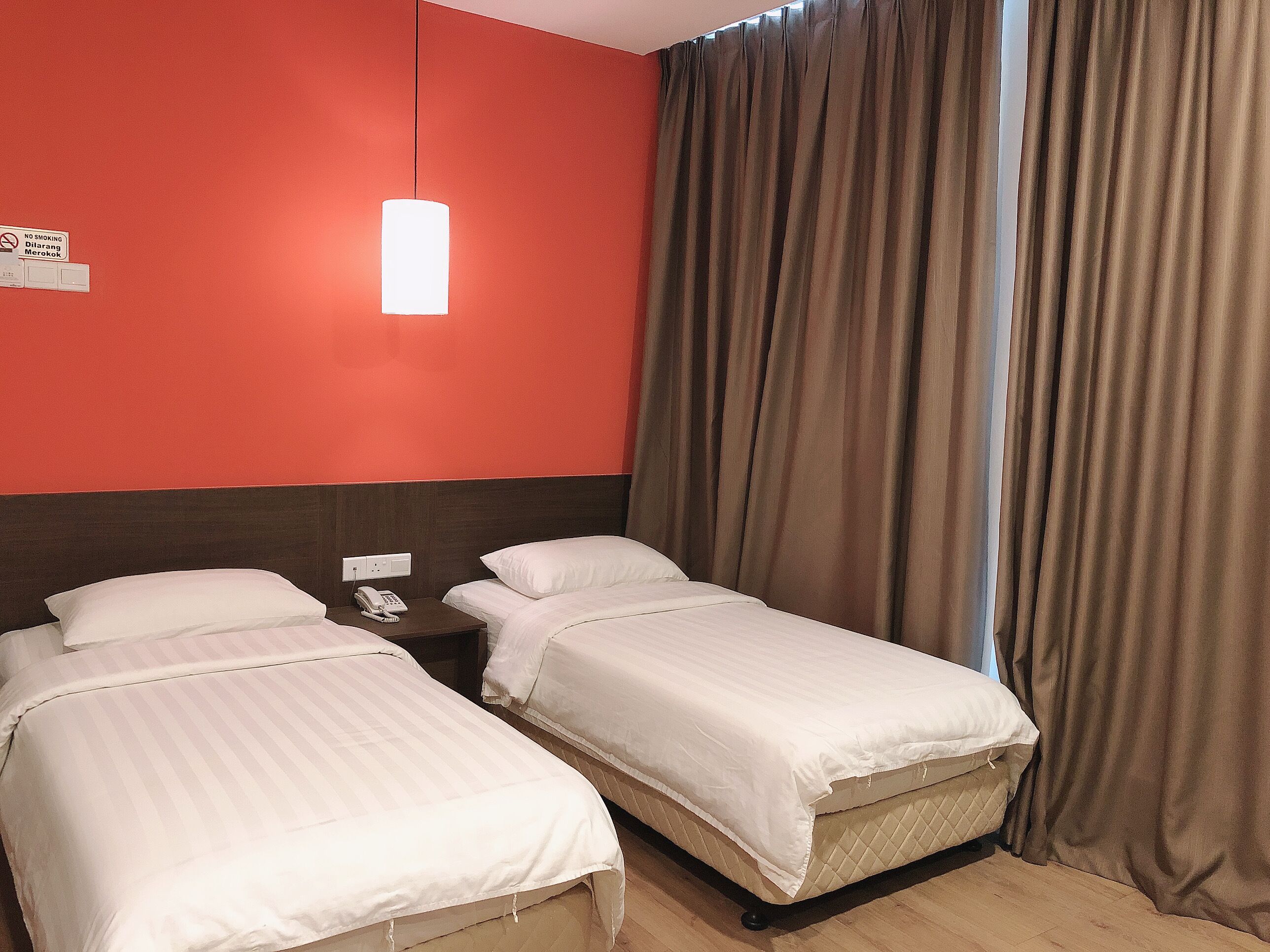 Habitación de hotel con dos camas, una mesita de noche con teléfono, pared roja y un ventanal con cortinas.