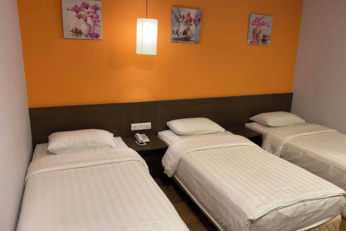 A hotel room with three single beds, a bedside telephone, and three floral paintings on the wall.