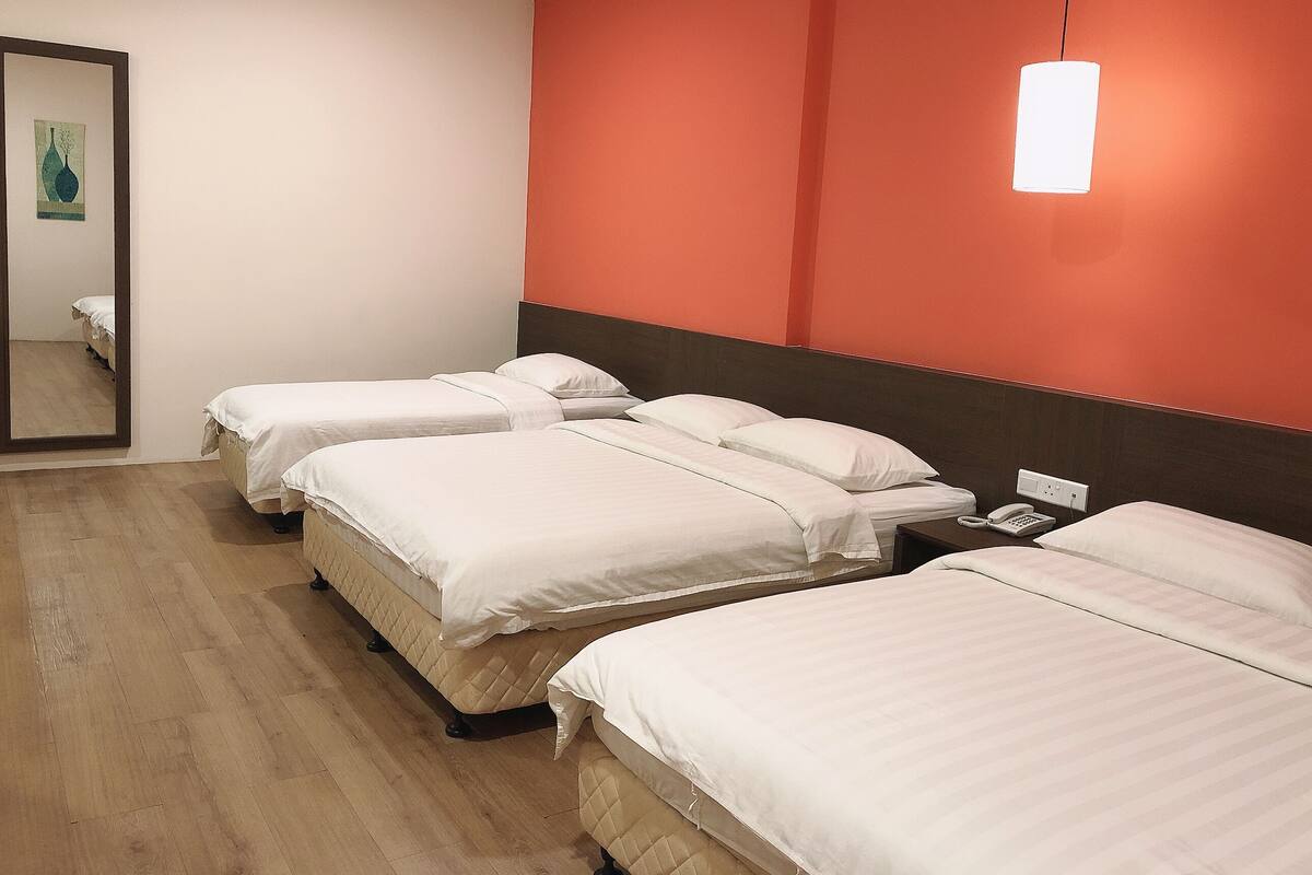 A hotel room with three beds, a wooden floor, a red accent wall, and a hanging light fixture.
