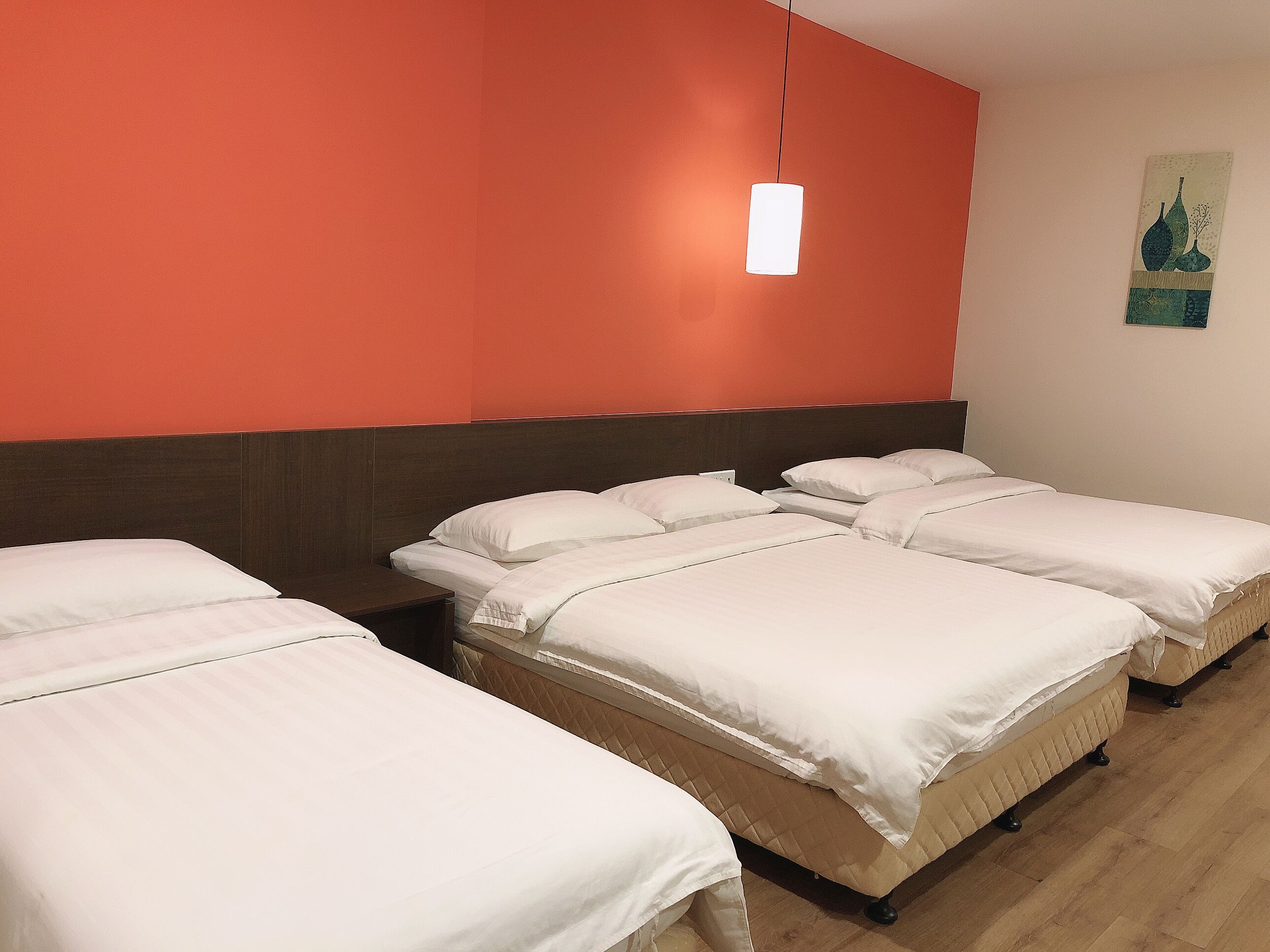 Una habitación de hotel con tres camas, un cabecero de madera y una lámpara colgante.