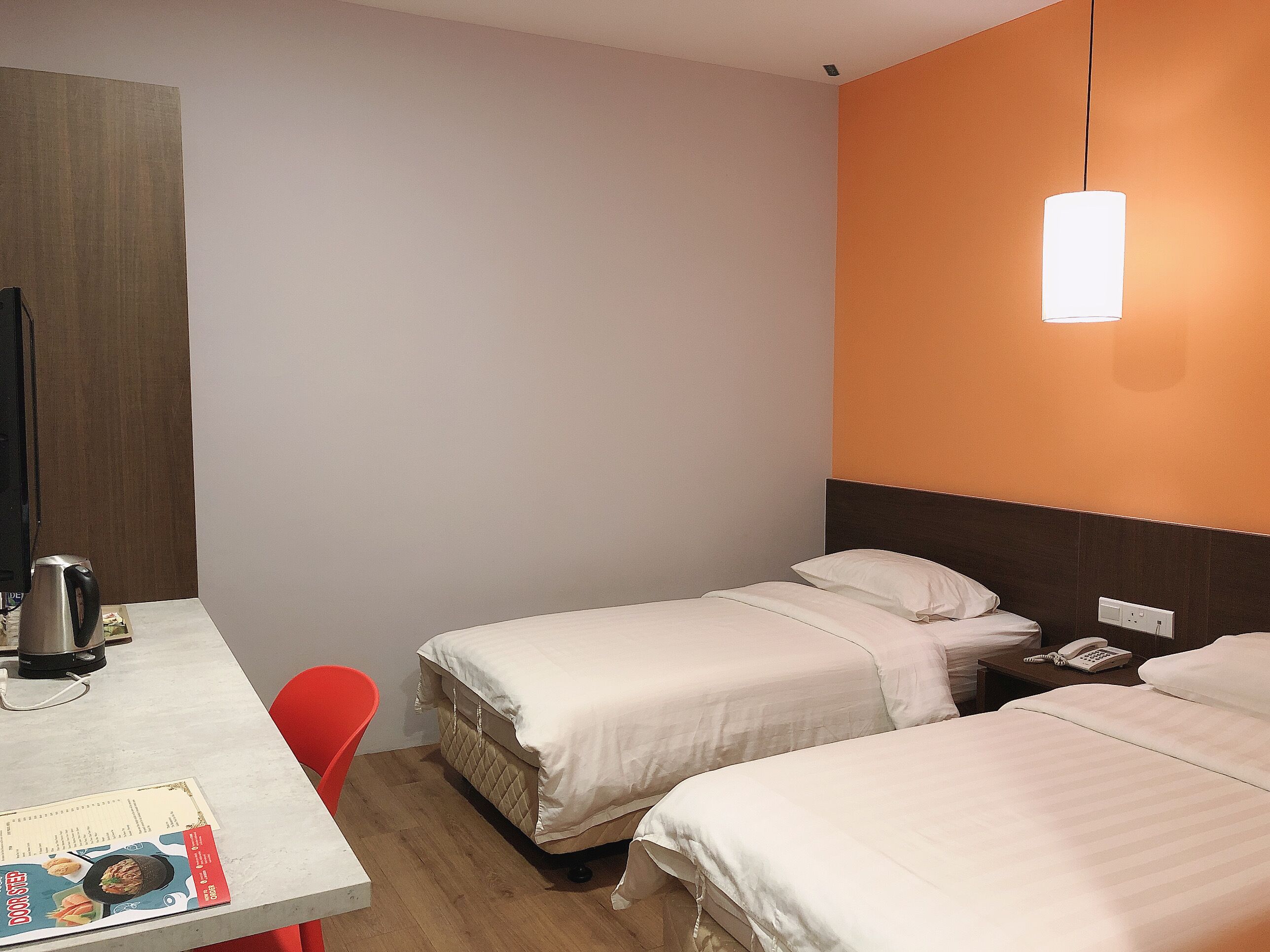 Habitación de hotel con dos camas, un escritorio con una tetera, una silla y una mesa con un menú.