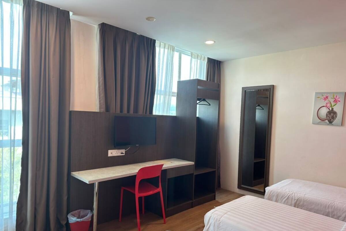 A hotel room with a bed, a desk, a chair, a TV, and a wardrobe.