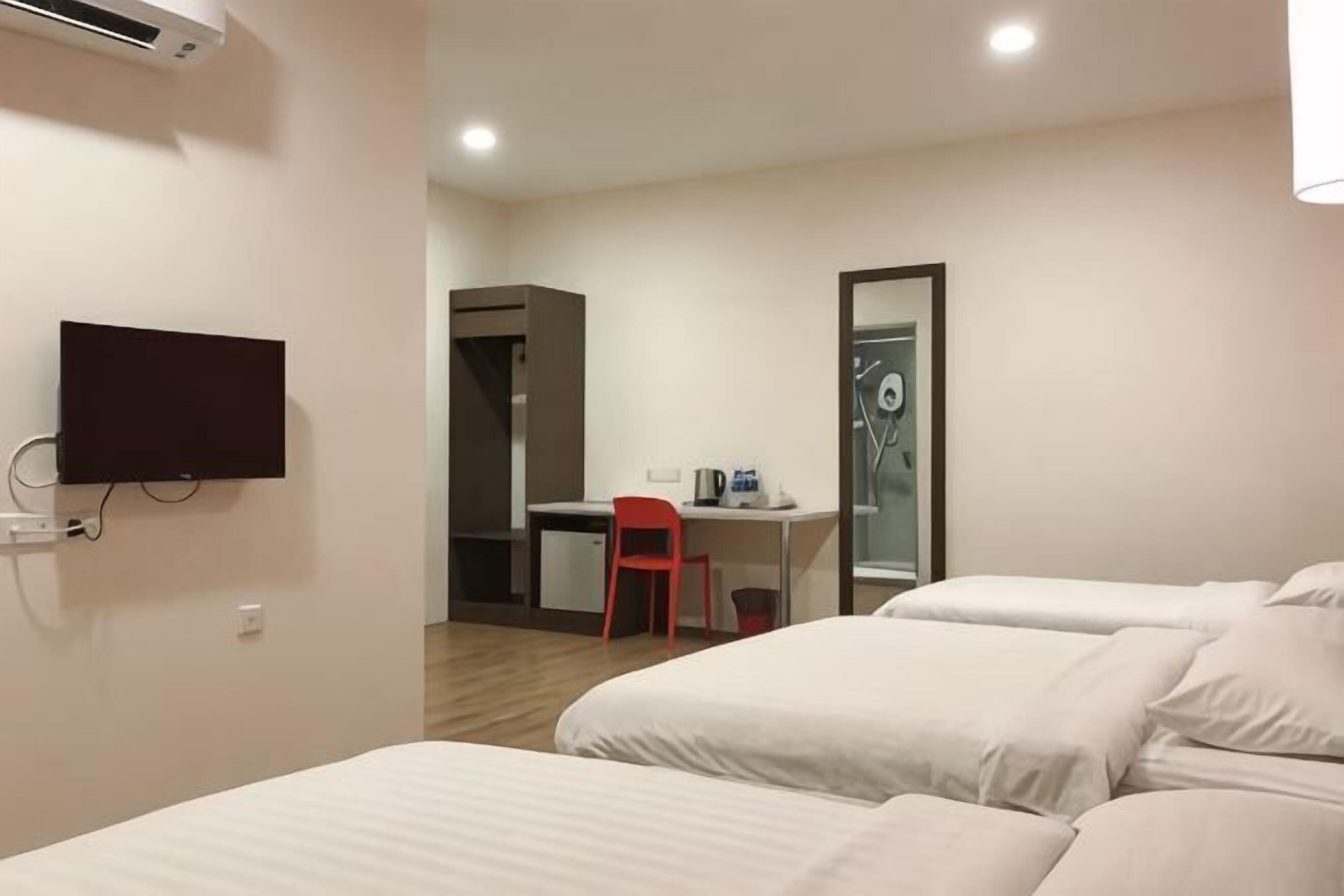 A hotel room with a bed, a desk, a chair, a TV, and a shower area.