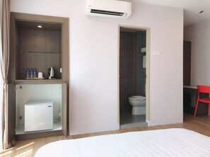 A hotel room with a bed, a wardrobe, a shower area, and a small desk with a chair.