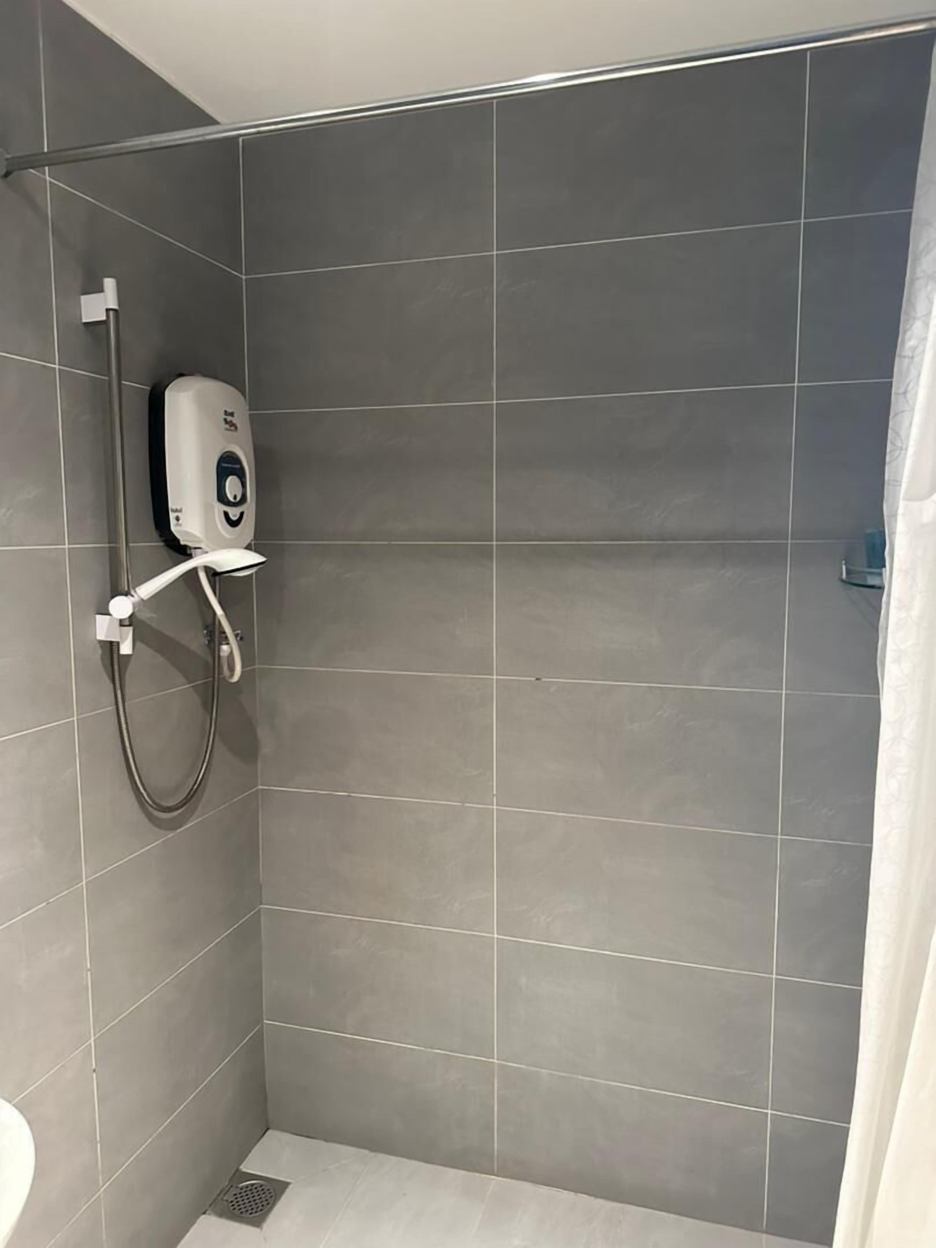 Zona de ducha con azulejos grises, un cabezal de ducha manual y un dispensador de jabón.