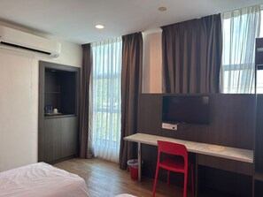 A hotel room with a bed, a desk with a chair, a TV, a wardrobe, and a window with curtains.