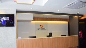 Un mostrador de recepción con el cartel GPI HOTEL, un televisor de pantalla plana y una zona de recepción de madera.