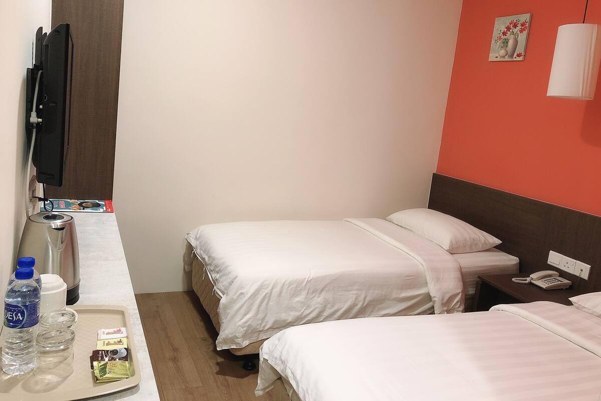 A hotel room with two beds, a bedside table with a phone, a water bottle, and a tray with snacks.