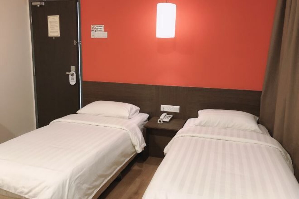 Ett hotellrum med två separata sängar, ett nattduksbord med en telefon och en vägg som är accentfärgad i rött.