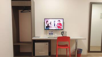 A hotel room with a bed, a desk with a computer, a red chair, a small fridge, and a mirror.