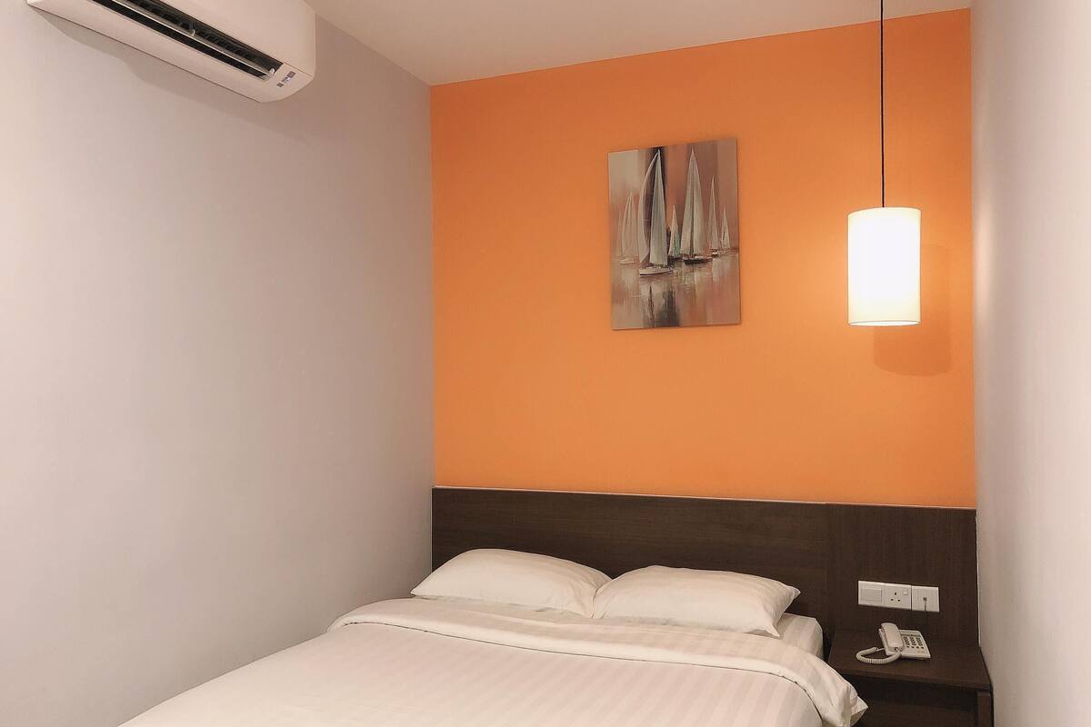 A hotel room with a bed, a nightstand with a phone, and a wall-mounted air conditioner.