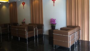 Un lobby moderno de hotel con sofás de cuero, una recepción y elementos decorativos tradicionales como adornos rojos y una planta en maceta.