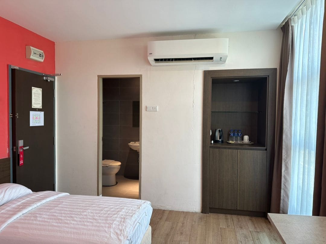 A hotel room with a bed, an air conditioning unit, a bathroom, and a kitchenette.