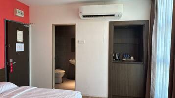 A hotel room with a bed, an air conditioning unit, a bathroom, and a kitchenette.