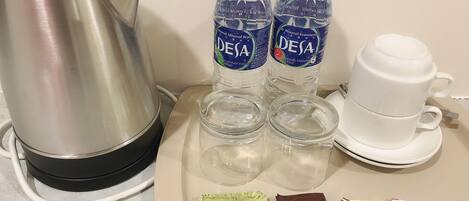 Una cocina equipada con un hervidor, dos botellas de agua, una cafetera y paquetes de té y café.