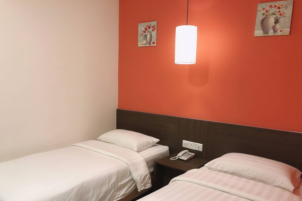 A hotel room with two single beds, a bedside table with a phone, and a wall-mounted light fixture.