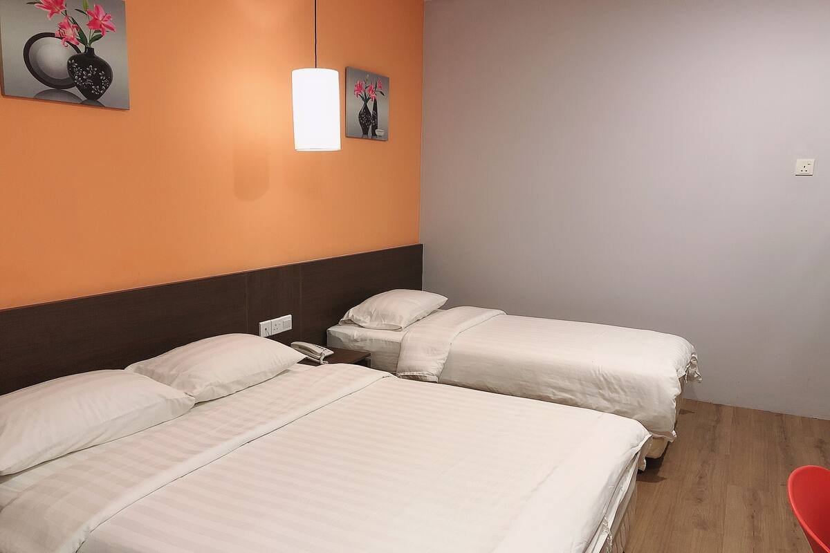 A hotel room with two beds, a bedside table with a phone, and a red chair.