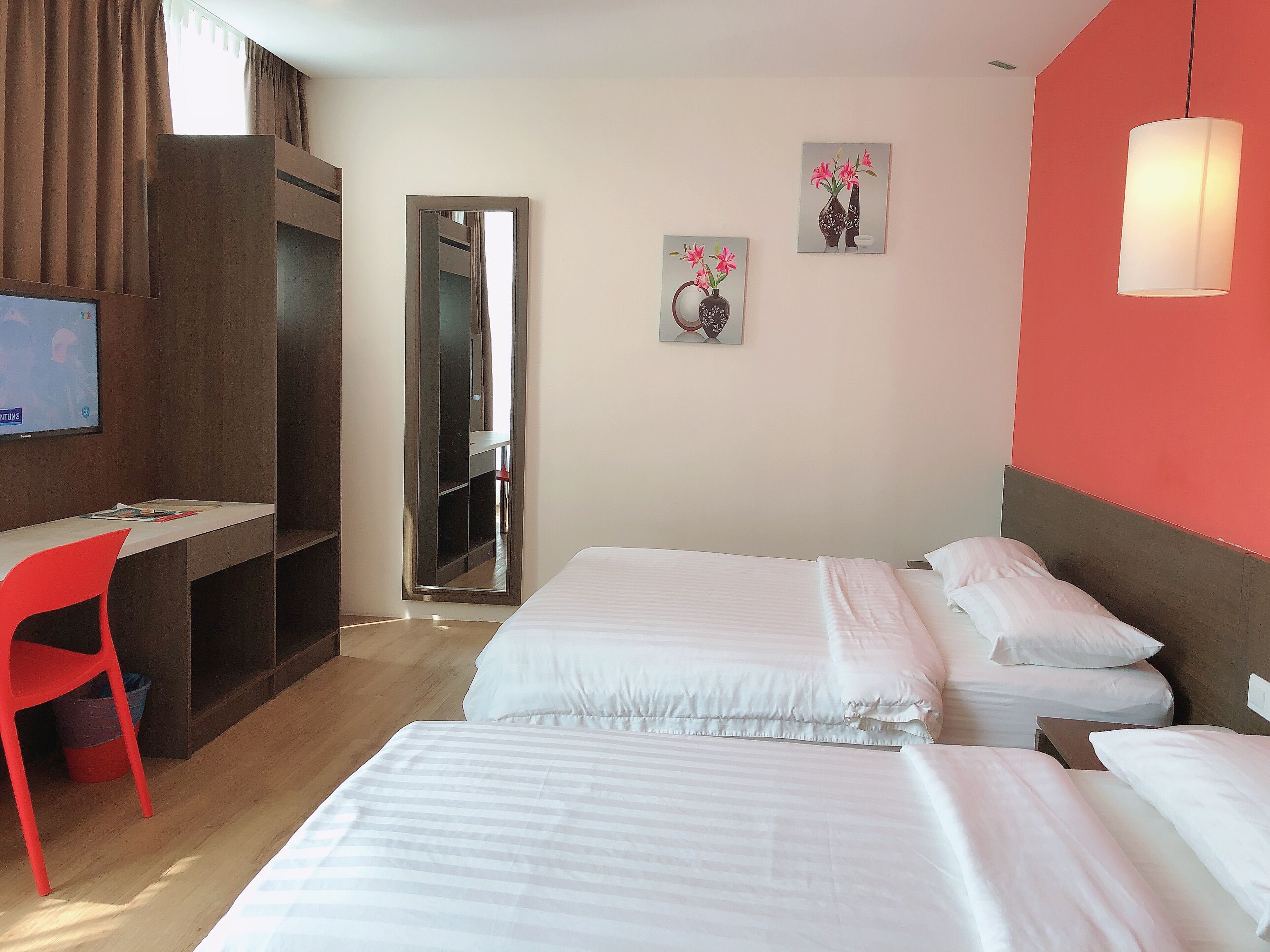 A hotel room with two beds, a desk, a chair, and a TV.