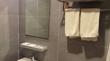 A bathroom with a sink, mirror, and toilet. There are towels on a rack and a trash bin.