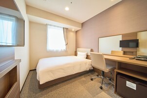 A hotel room with a bed, a desk, a chair, a TV, and a minibar.
