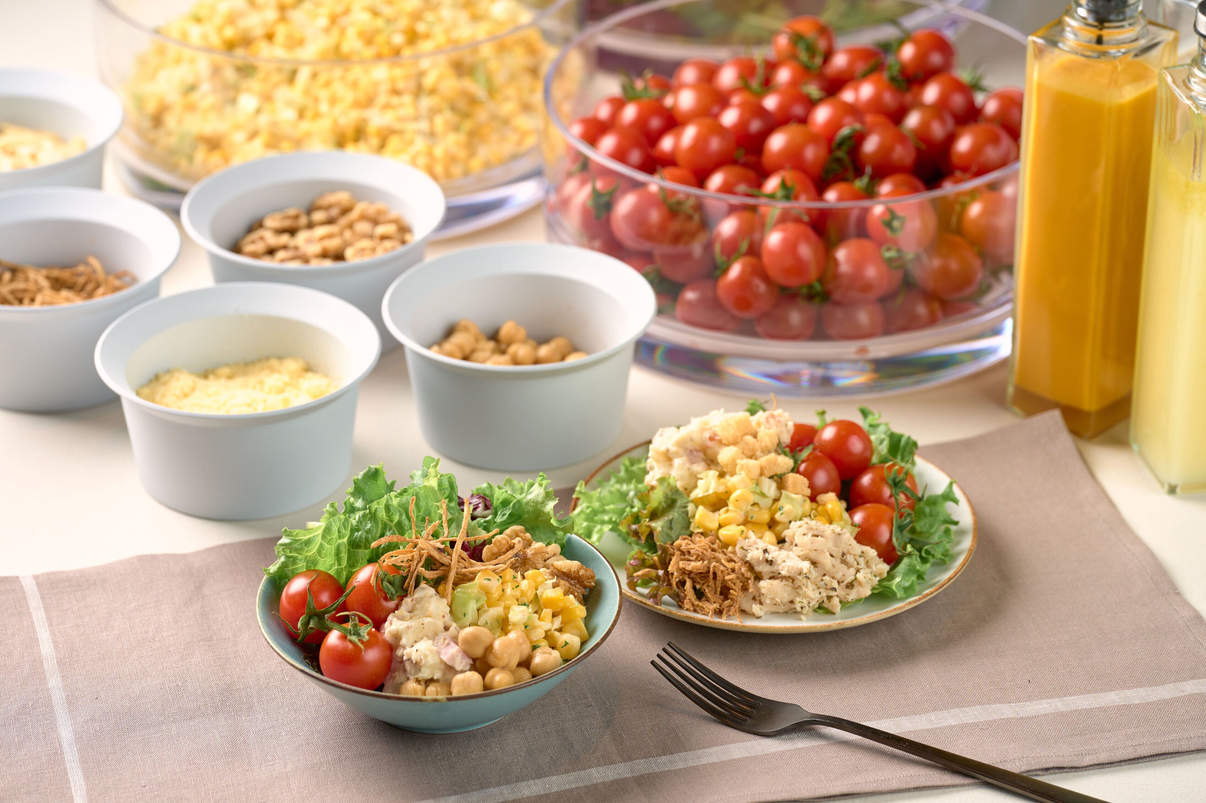A table with various food items including salads, bowls of nuts, and a container of cherry tomatoes.