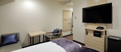 A hotel room with a bed, a desk, a chair, a TV, and a small cabinet.
