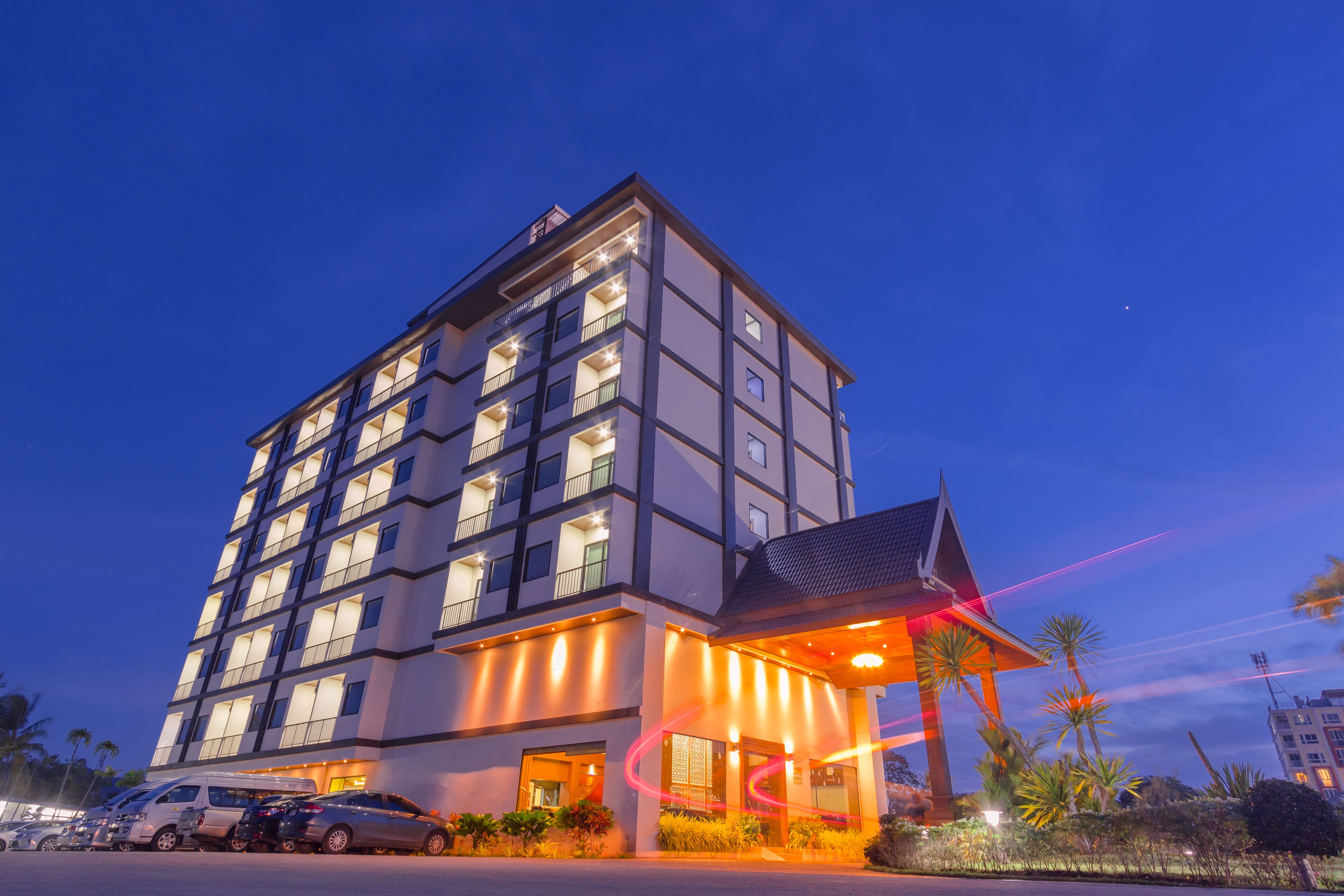 A multi-story hotel with a modern design, featuring a prominent entrance with a covered area and a visible parking lot with several cars.