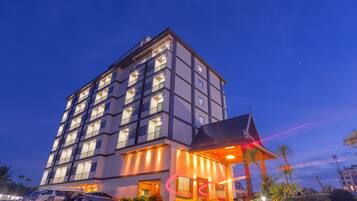 A multi-story hotel with a modern design, featuring a prominent entrance with a covered area and a visible parking lot with several cars.