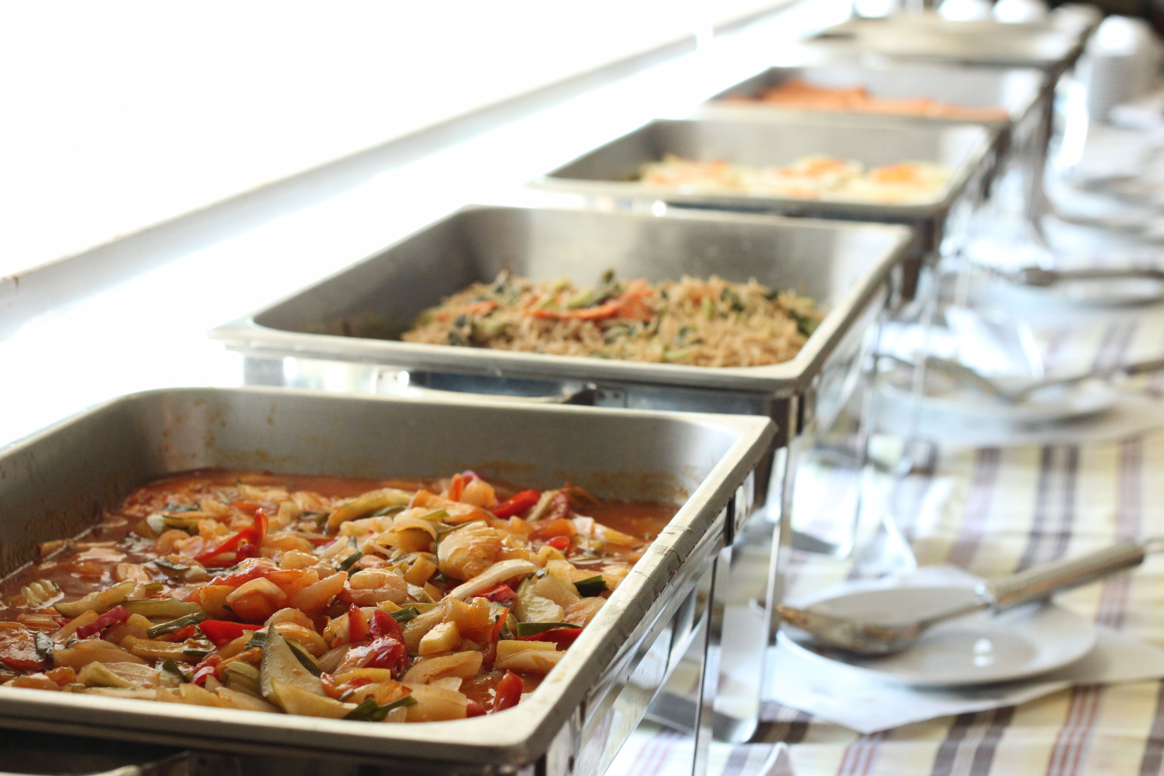 A buffet line with various dishes, including a vegetable stir-fry and a rice dish.