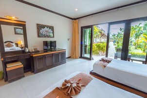 A hotel room with a bed, a desk, a television, and a view of a garden.