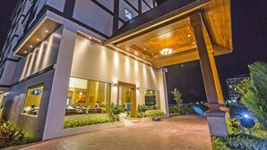 A modern hotel entrance with a covered outdoor area, a reception desk, and visible windows.