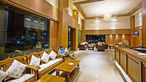 A spacious lobby with wooden furniture, a reception desk, and a large window overlooking the street.