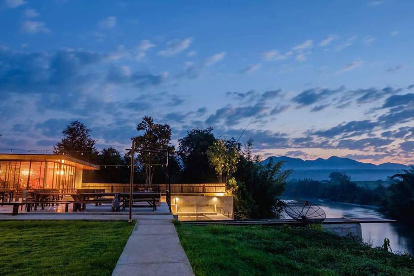 A modern building with a glass facade, outdoor seating, and a river view.