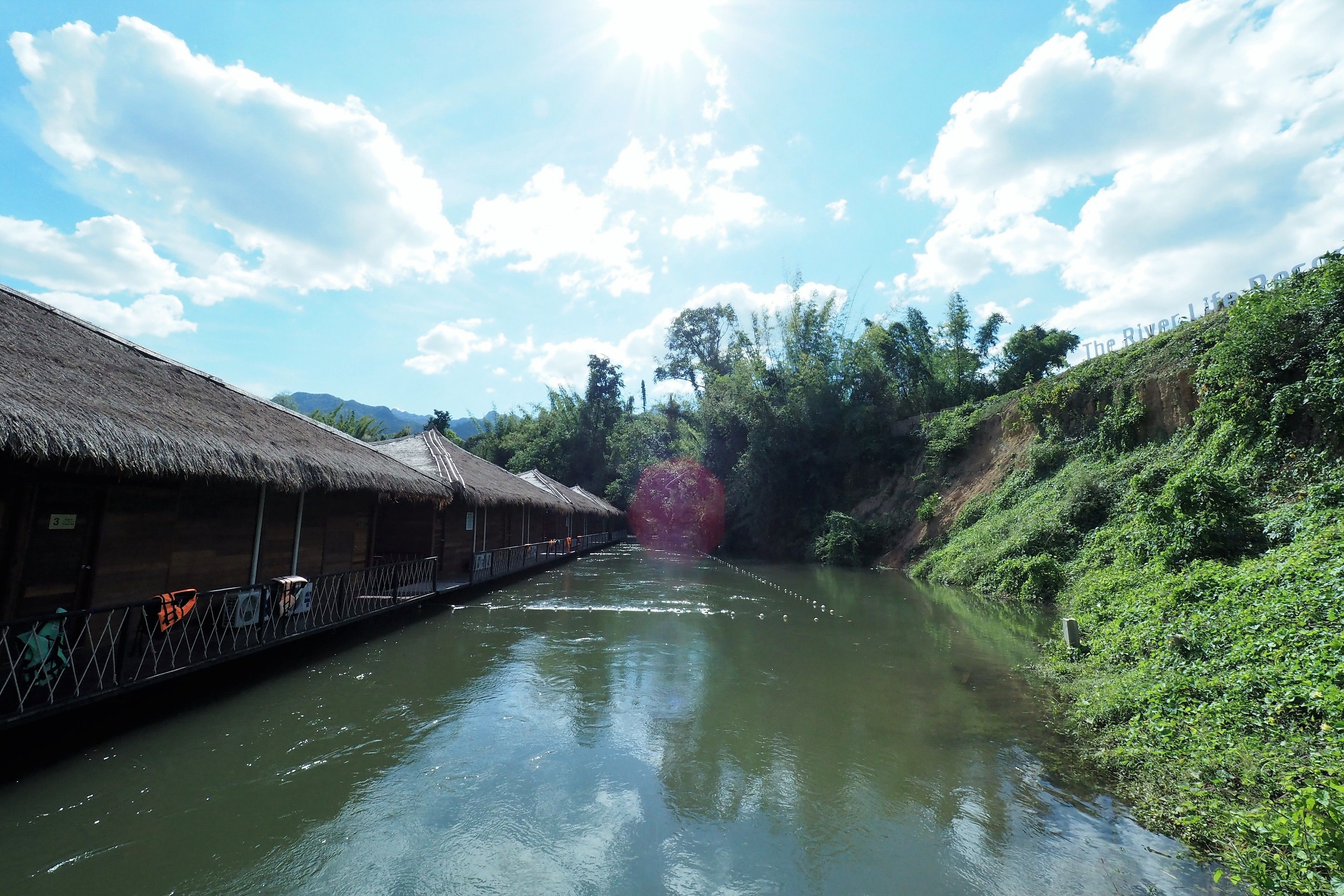 Un río con una pasarela de madera a la izquierda, rodeado de follaje y árboles.
