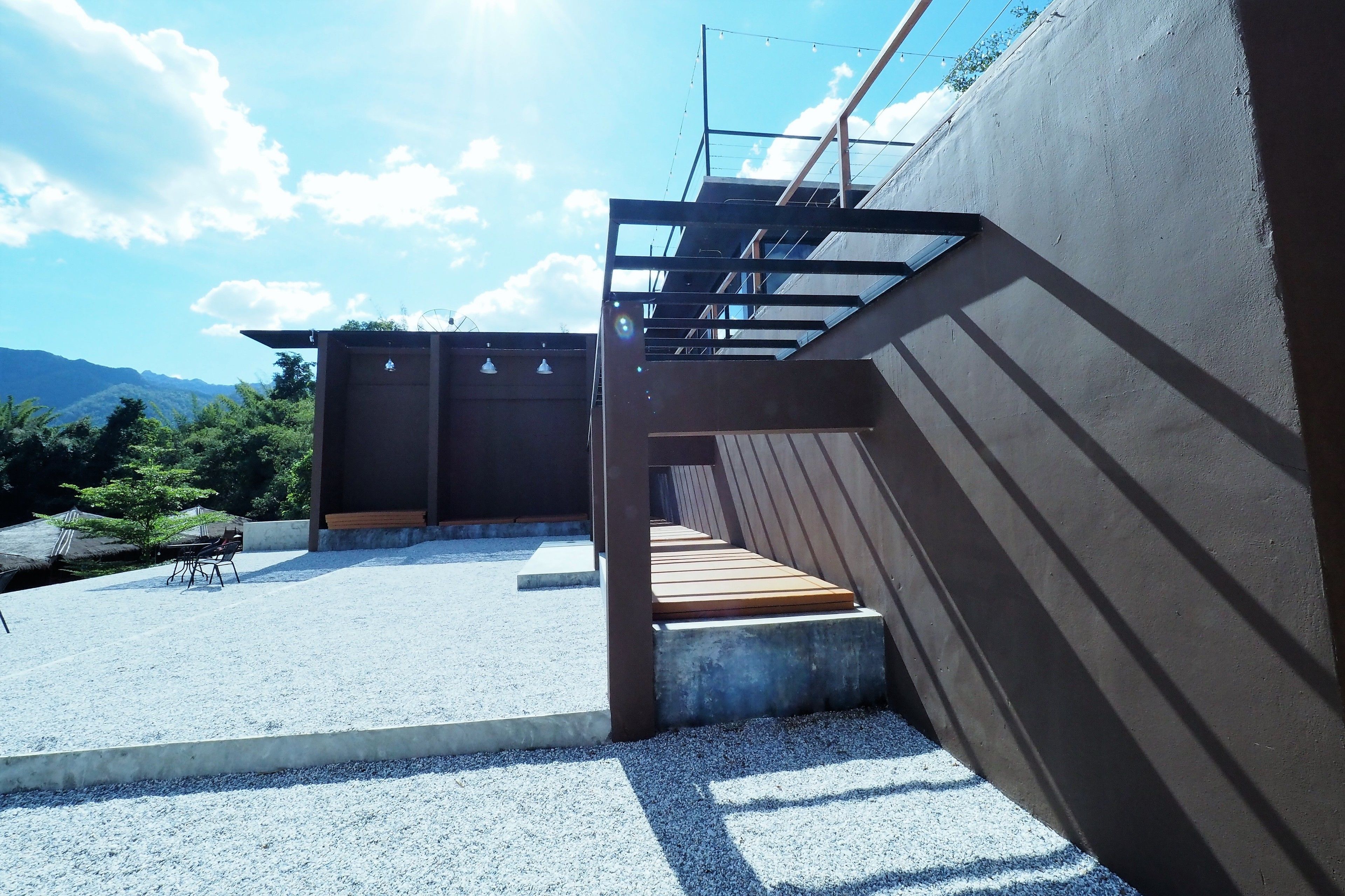 A modern outdoor terrace with a concrete floor, wooden steps, and a metal railing.