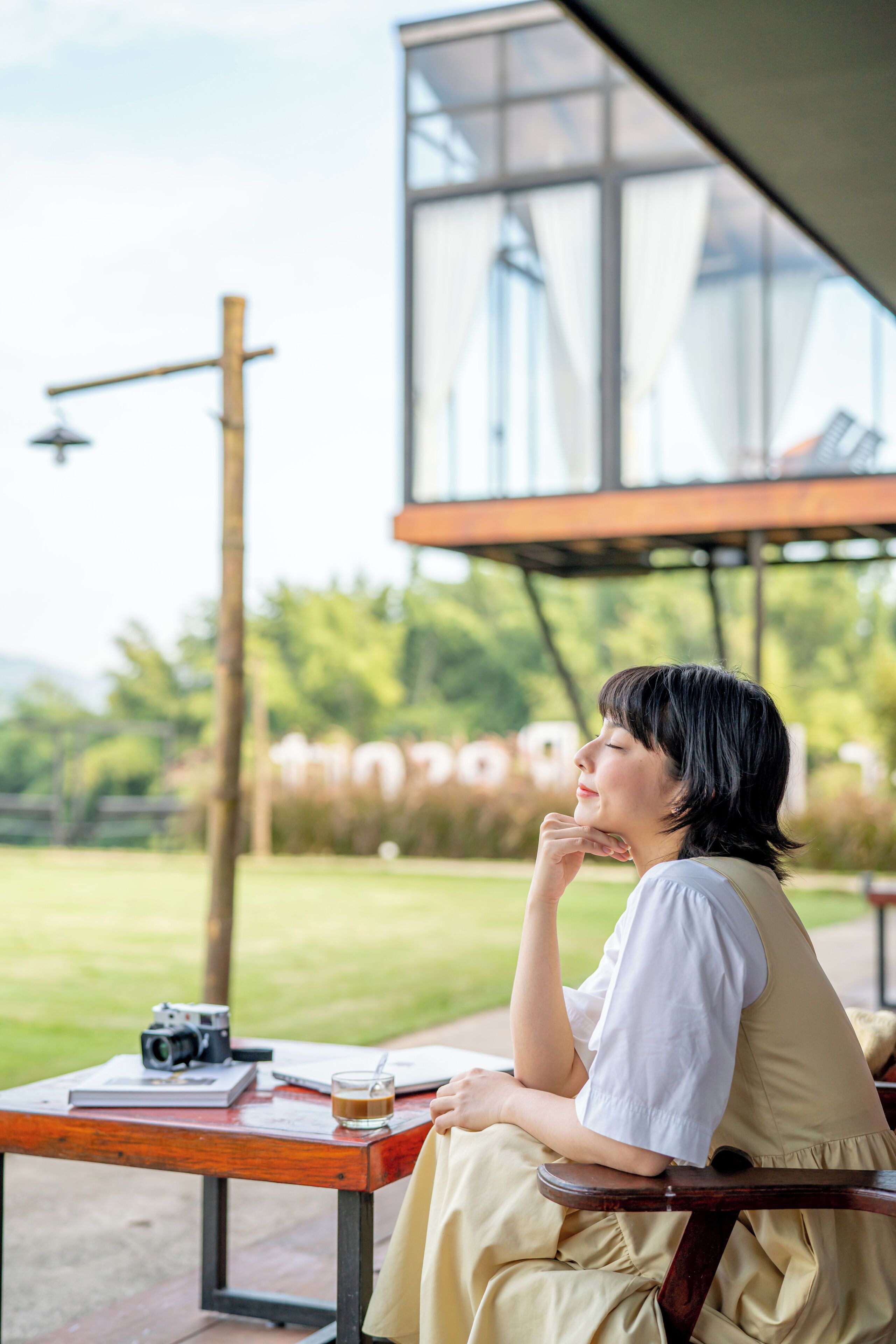 A person sitting at an outdoor table with a camera and a glass of drink.