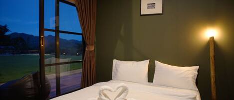 A hotel room with a bed, a framed picture on the wall, and a view of the outdoors through a large window.