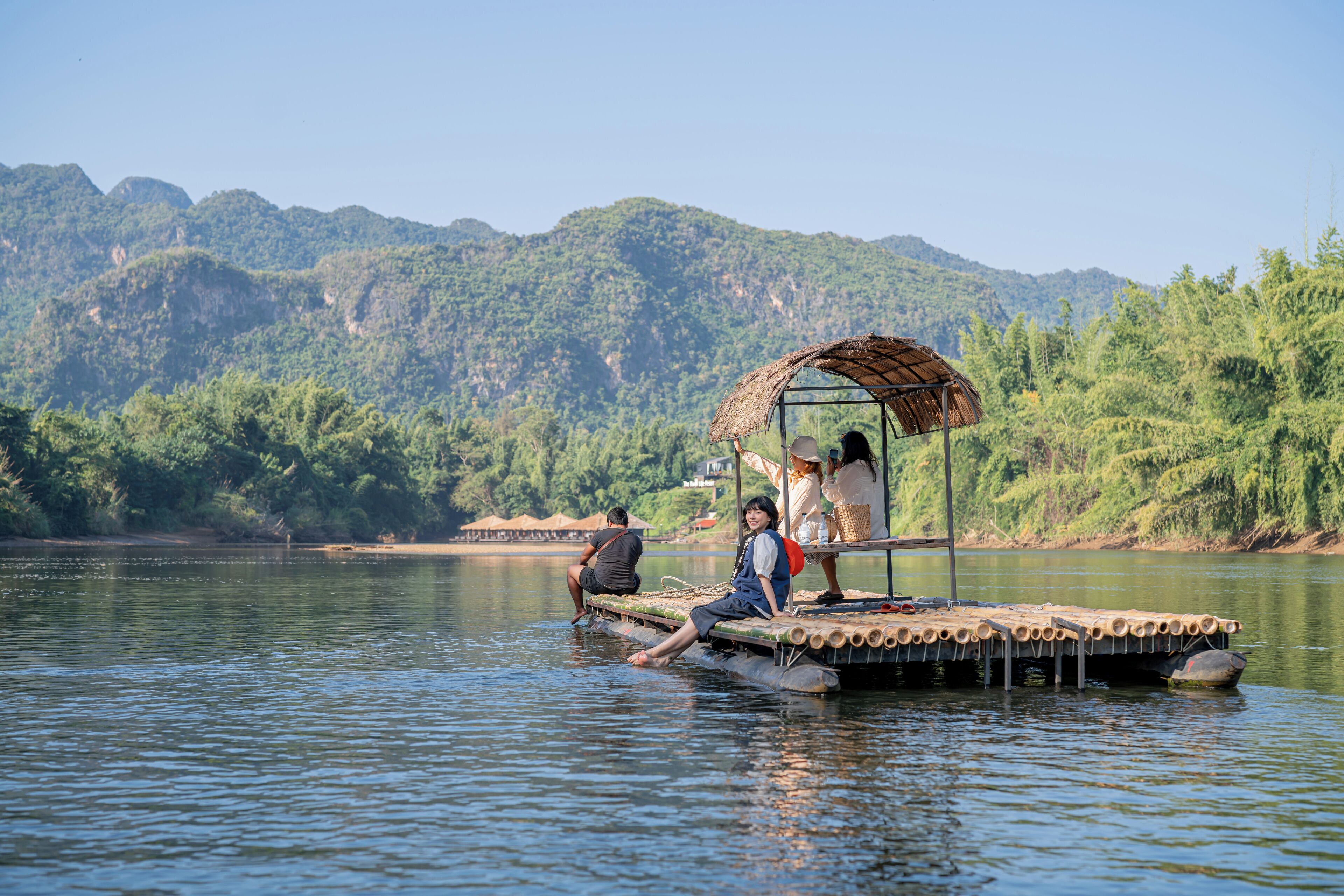 A floating structure with a thatched roof, surrounded by calm water and lush greenery.