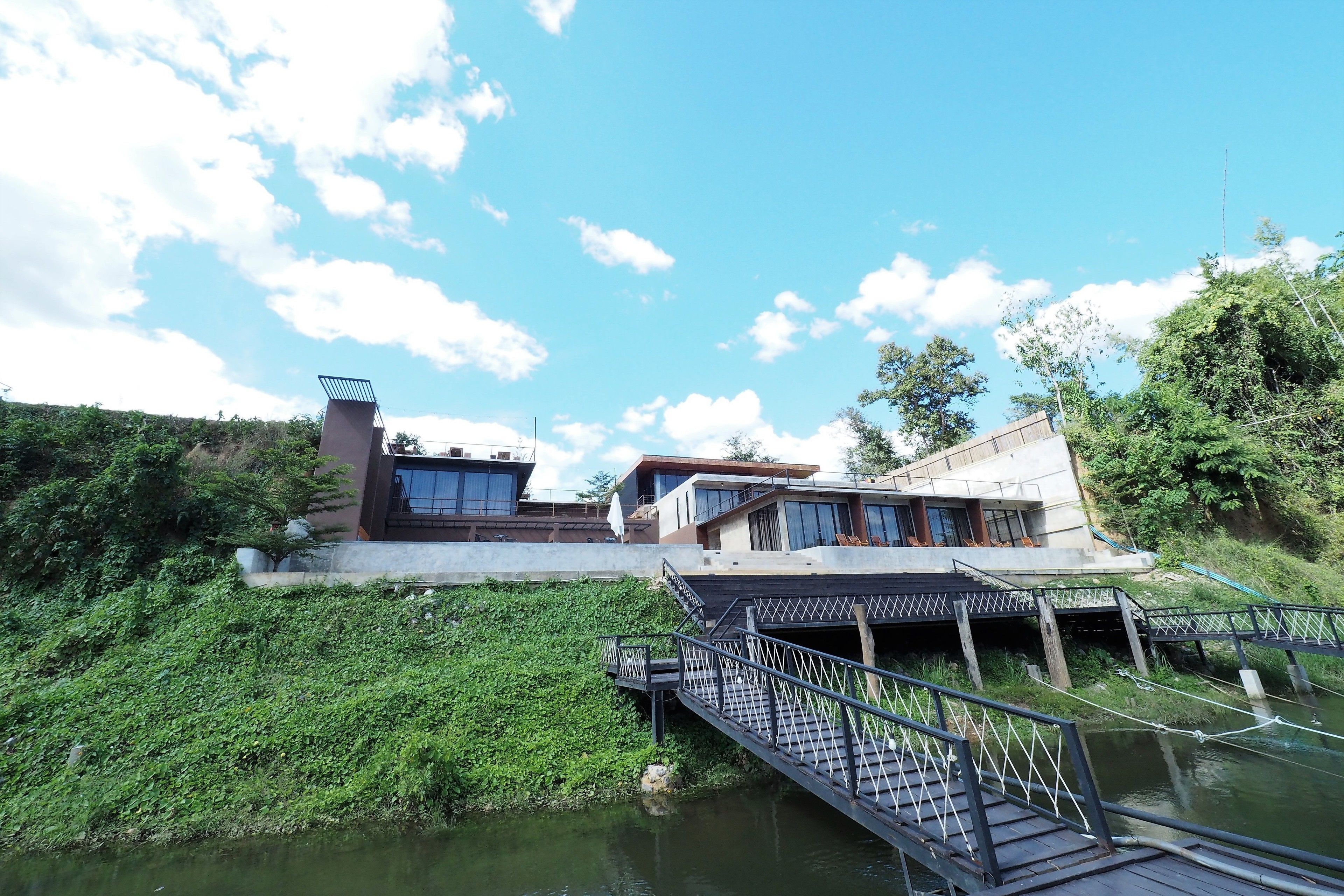A modern building with a bridge over a body of water, surrounded by greenery.