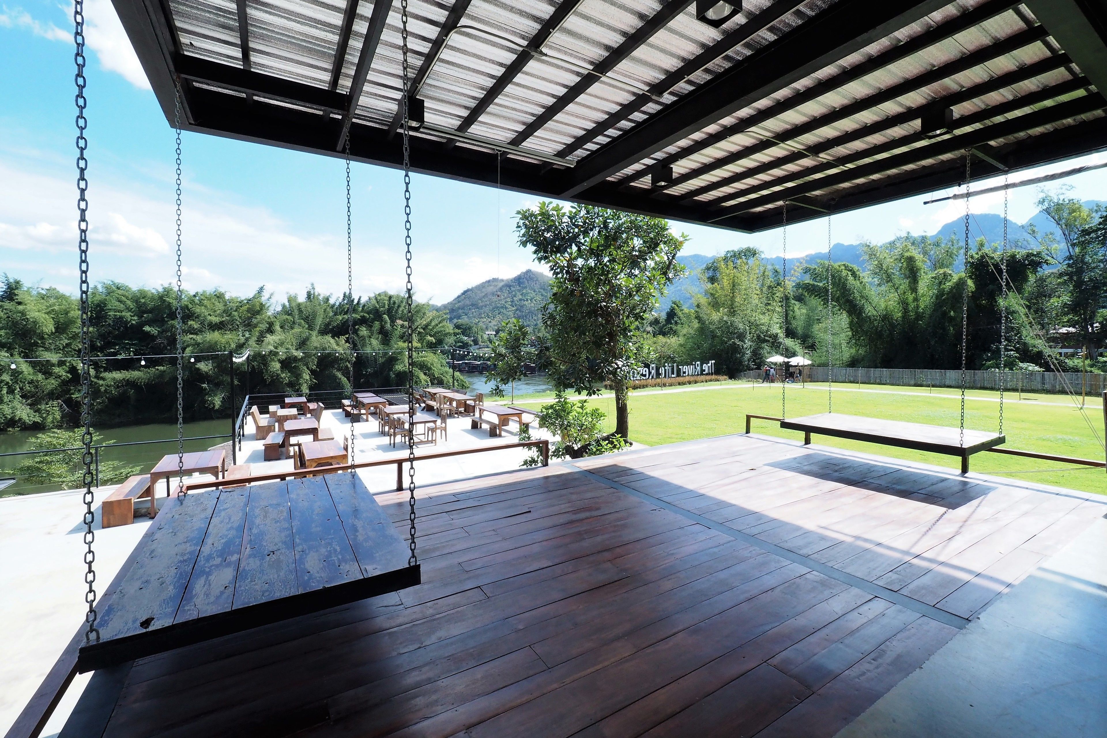 Un espacio de estar al aire libre cubierto con bancos y mesas de madera, con vistas a un río y montañas.