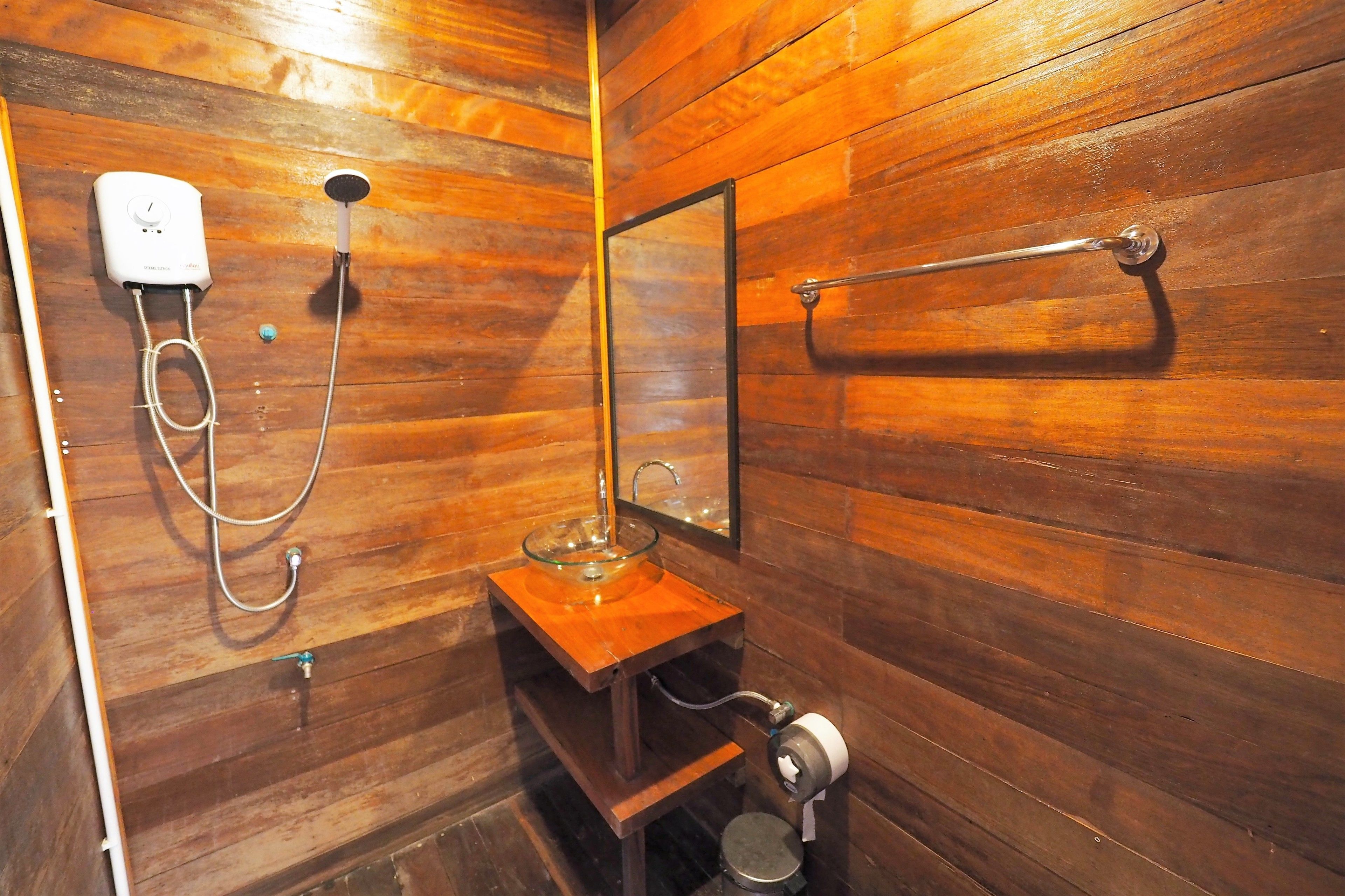 Un baño con paneles de madera, un lavabo de vidrio, un cabezal de ducha manual y un perchero para toallas.